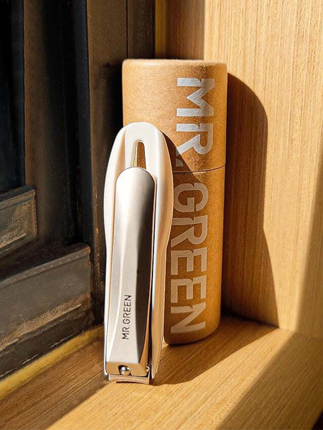 MR.GREEN anti-splash stainless steel fingernail clipper with clippings catcher and ergonomic handle beside branded kraft tube in sunlight — precision nail cutter